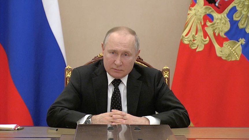 Russian President Vladimir Putin seated.
