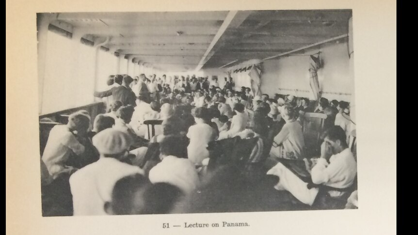 black and white photo of a large group of people seated on a ship's deck, from behind