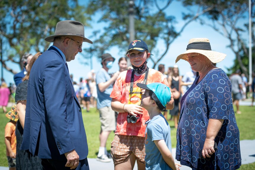 anthony Alabanese stands in a suit and hat and talks to two children and a woman outside at an event in Darwin