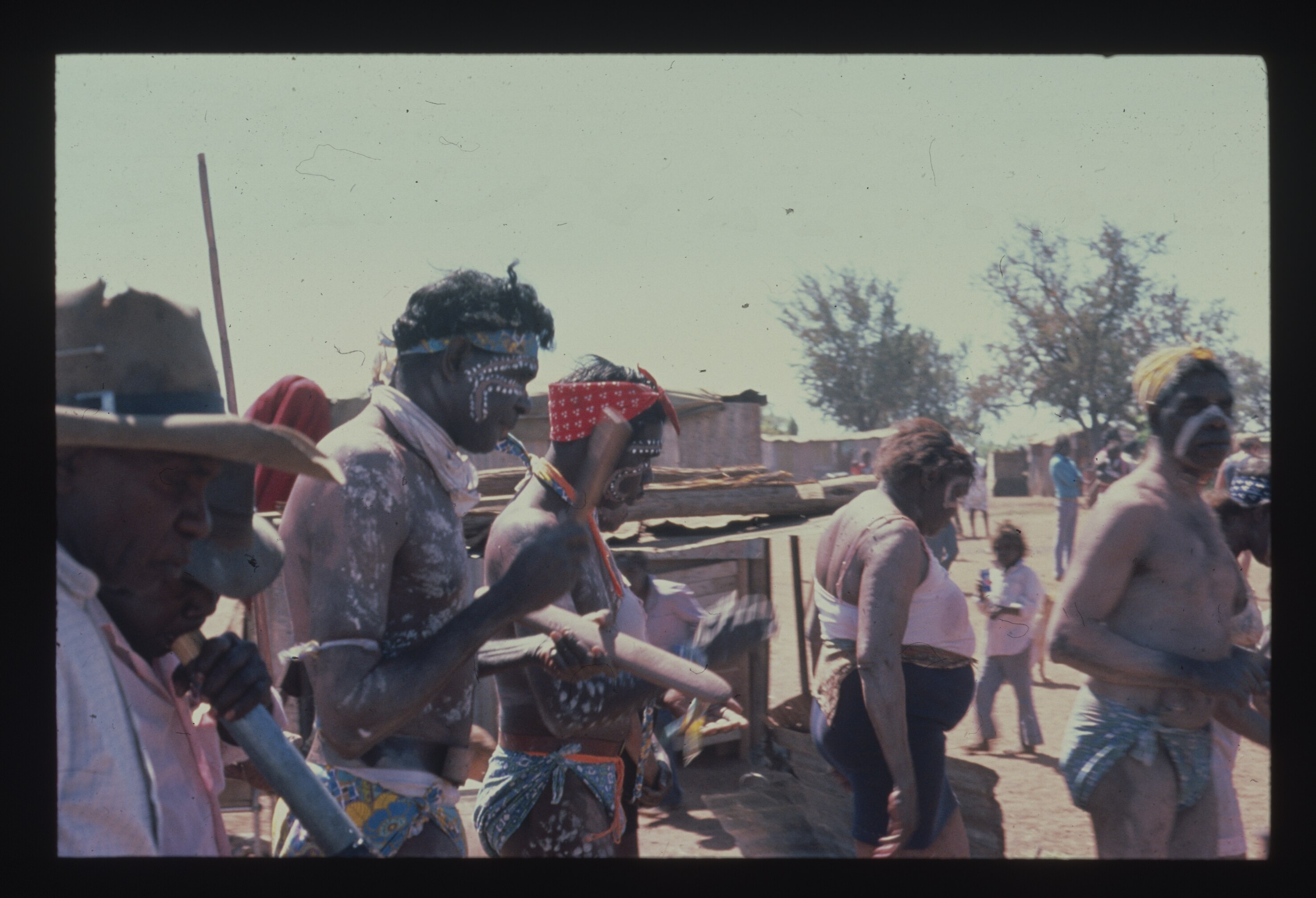 A group of Aboriginal people performing with clap sticks and didgeridoos in remote appearing town.