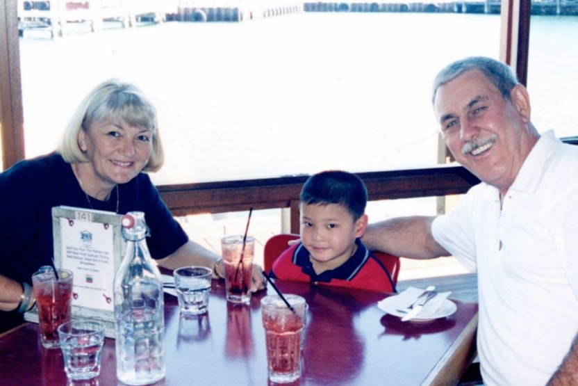 A young Asian boy sits between his two parents at a table. They all smile.