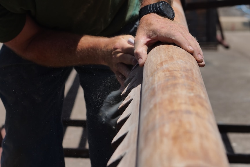 close up of hands working on long piece of wood. 