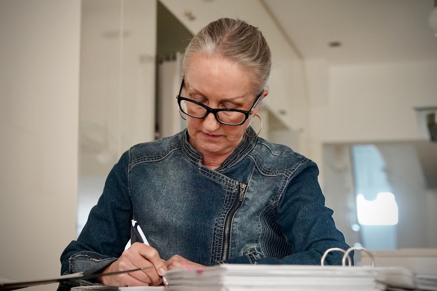 A woman with glasses writing with a pen
