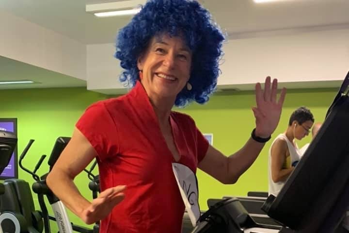 A woman participates in a fundraiser, wearing a blue wig on a treadmill.