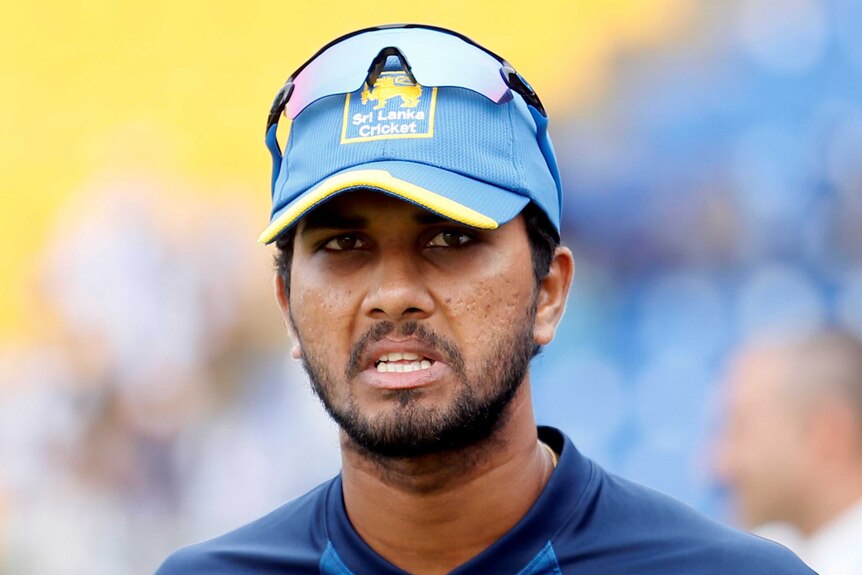 A glum looking young man with a short cropped beard wears his sunglasses atop of his blue Sri Lanka Cricket cap