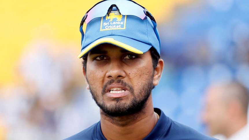 A glum looking young man with a short cropped beard wears his sunglasses atop of his blue Sri Lanka Cricket cap