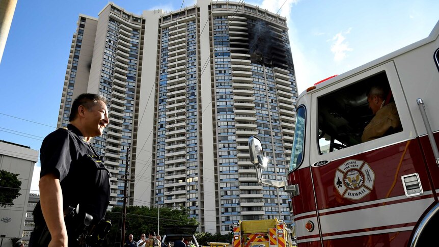 A police officer directs a fire truck at the Marco Polo apartment building after a fire broke out in it in Honolulu,