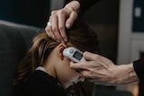 Close up of an adult's hand holding an in-ear thermometer to a child's ear.