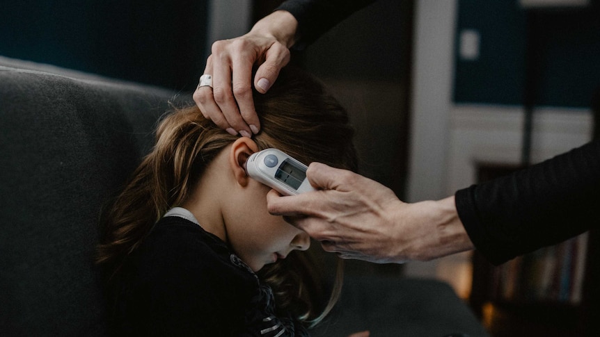 Close up of an adult's hand holding an in-ear thermometer to a child's ear.