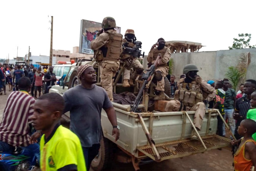 Malian troops in the back of a pickup truck and citizens gather outside the private residence of Mali's President.