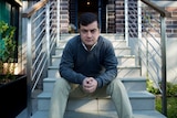 SAm Dastyari sits with his hands resting on his knees while he sits at the bottom of a set of exterior stairs