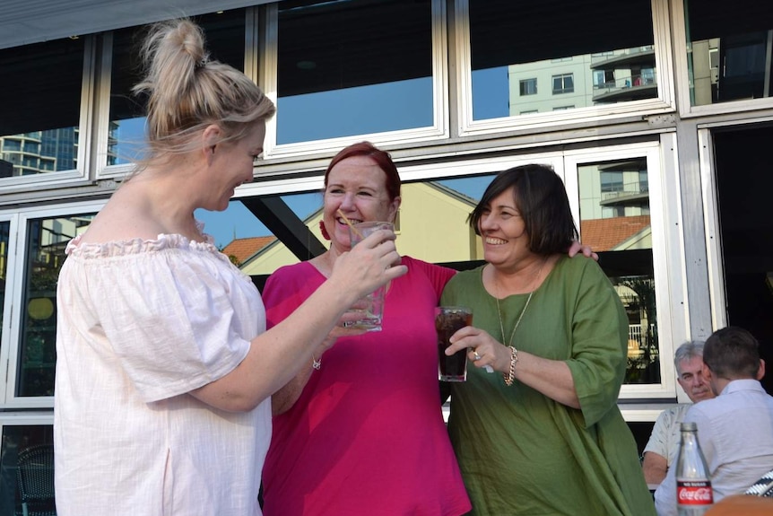 A group of women smiling and clinking glasses at a pub