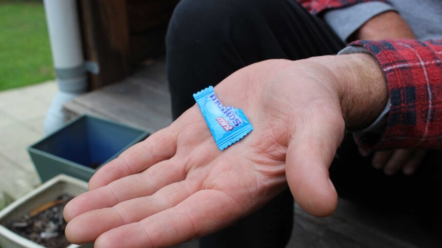 A close up shot of a man's hand holding a plastic Mentos mint wrapper.