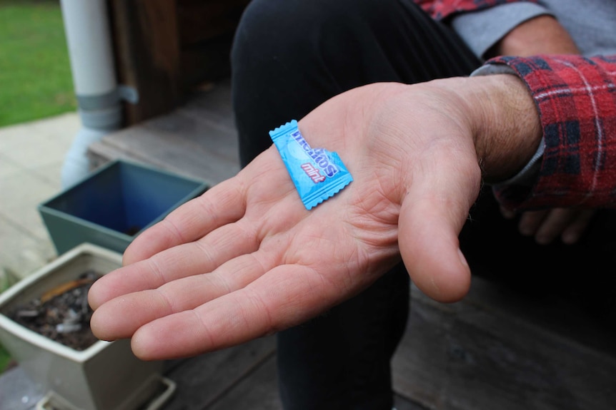 A close up shot of a man's hand holding a plastic Mentos mint wrapper.