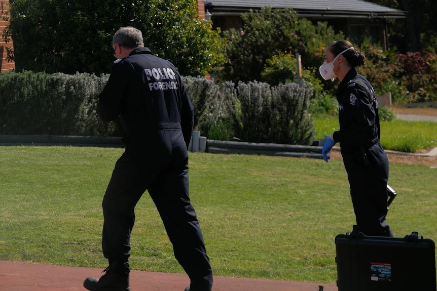 Two police officers wearing forensics jumpsuits approaching a crime scene