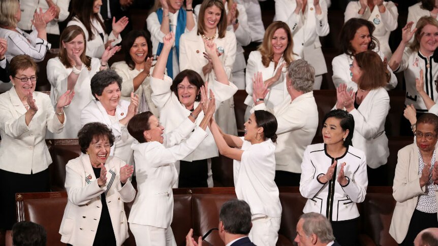 Women wearing white cheering and high-fiving each other.