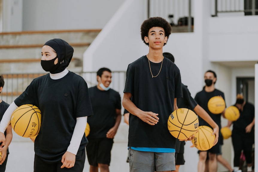 Afghan refugee Sabera and a teenage boy hold basketballs and stand on an indoor court.