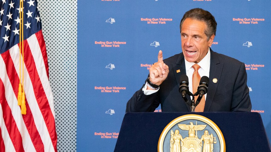 Andrew Cuomo speaks behind a lectern with a finger raised in the air.