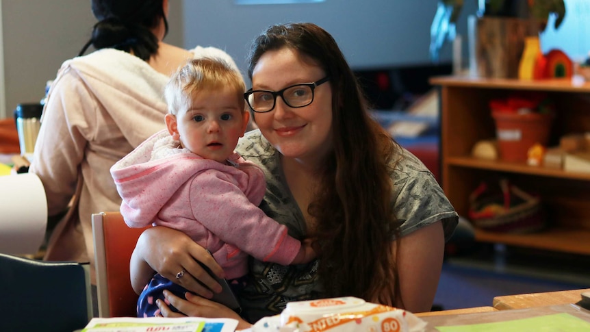 A young woman holds her baby in a classroom