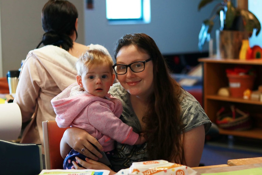 A young woman holds her baby in a classroom