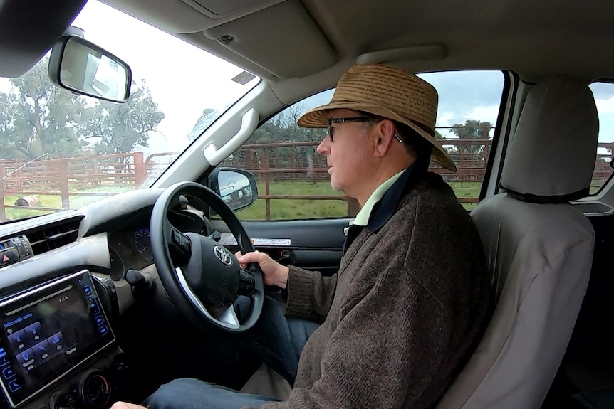 A side profile of a man in an Akubra-style hat at the wheel of a car.