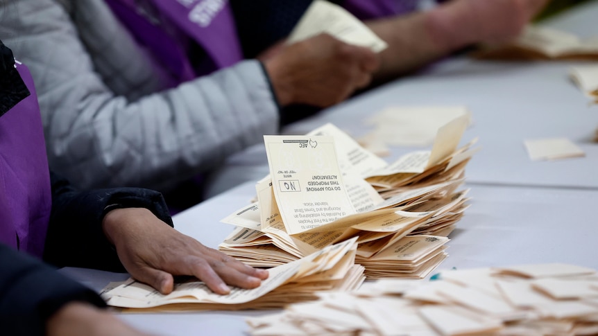 a close up of people's hands sorting ballot papers, with a focus on one that says "no"
