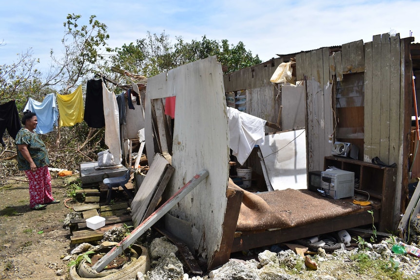 A woman looks at a property that is barely recognisable as a house.