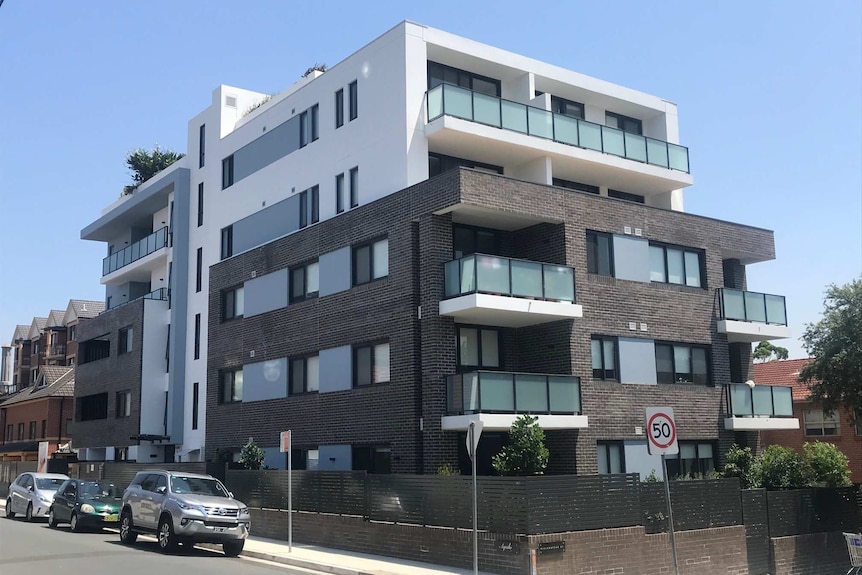 An apartment block with dark bricks and white balconies on a corner block