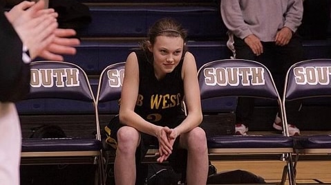 A young girl sits on a bench next to a basketball court.