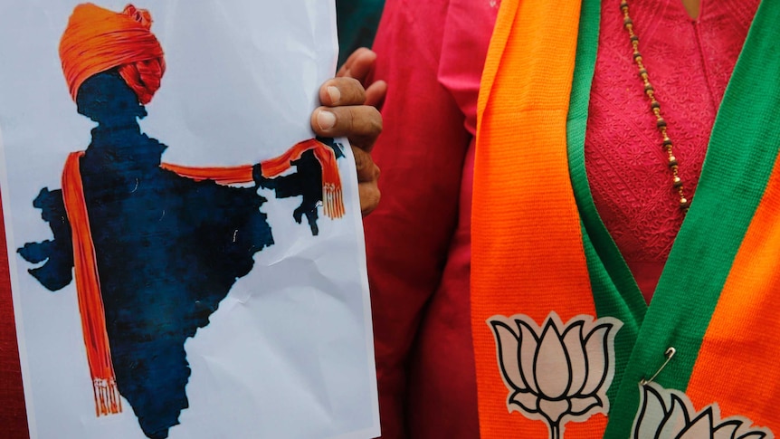 A close up photo shows someone holding an illustrated map of India donning an orange turban shawl, next to a woman.