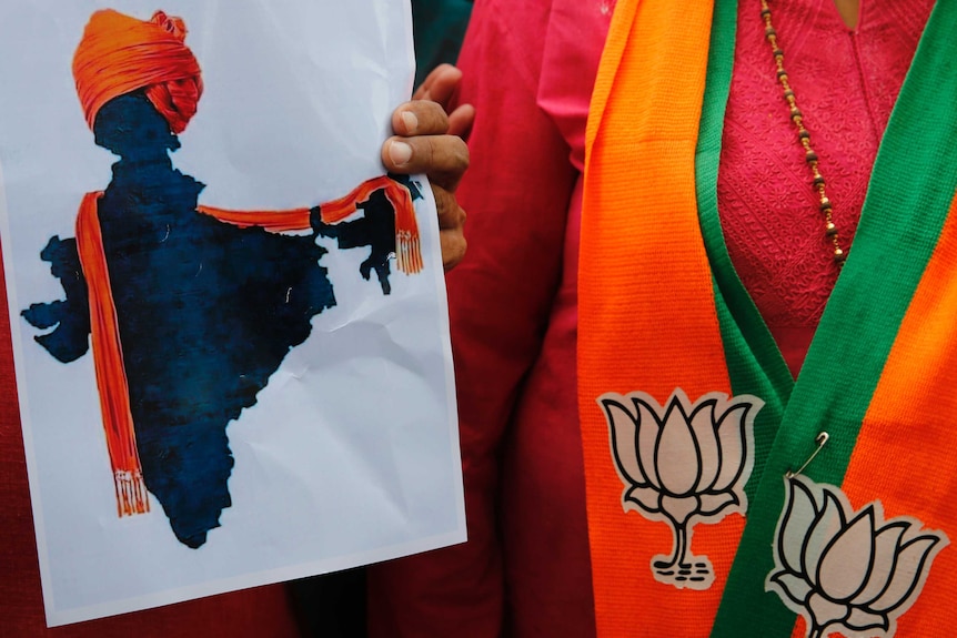 A close up photo shows someone holding an illustrated map of India donning an orange turban shawl, next to a woman.