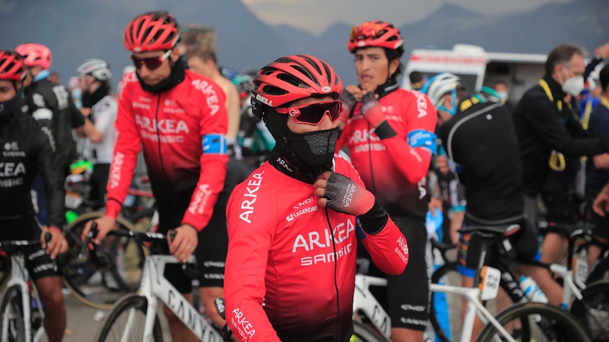 Three cyclists wear red cycling kit that fades to black in a group of other cyclists