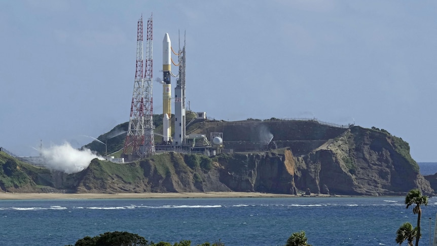 A space rocket launch vehicle on a rocky island, the picture is taken across the water from the mainland