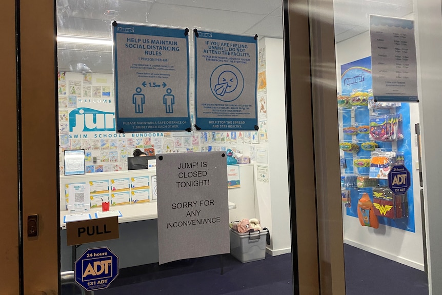 The window of a swim school with signs explaining that it's shut.