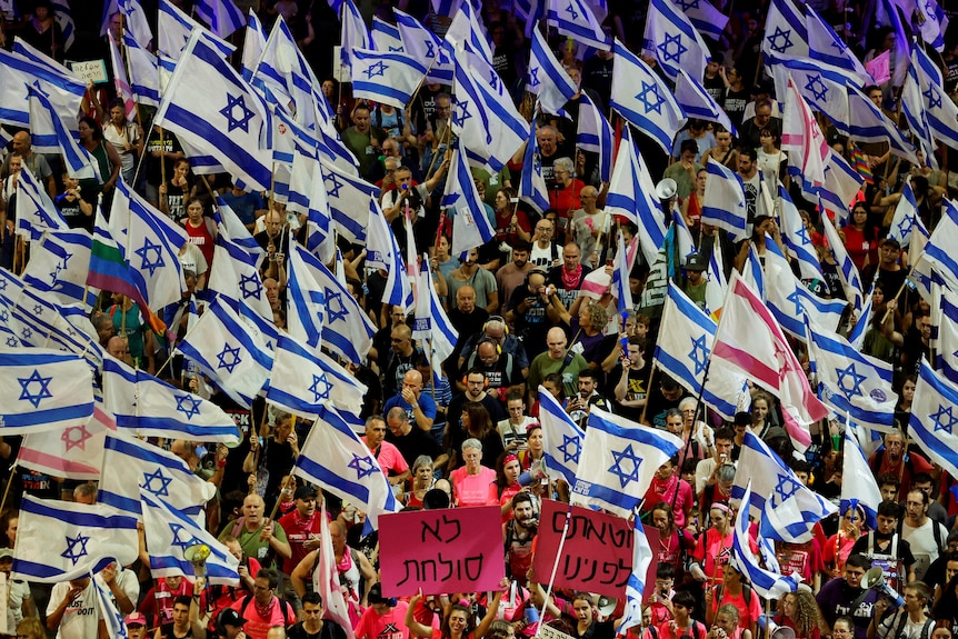 A crowd of people walk holding Israeli flags and signs.