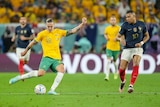 Australia's Jackson Irvine looks down at the ball as he hits it with his right foot, while France's Kulian Mbappe watches.