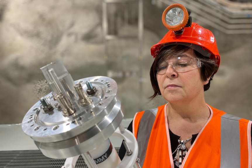 A woman holds a piece of scientific equipment in an underground lab