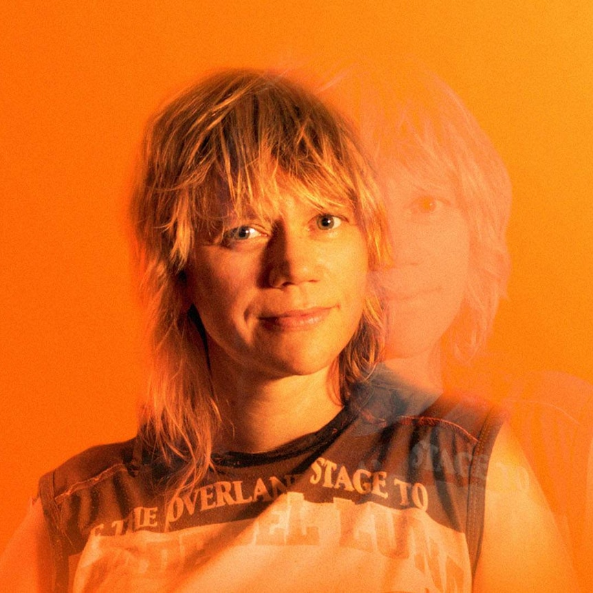 Liz Martin with blonde hair with a fringe against an orange background. A ghost of her image is doubled to the side
