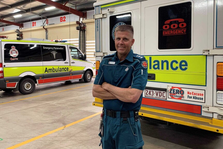A man stands with his arms crossed in front of an ambulance van.