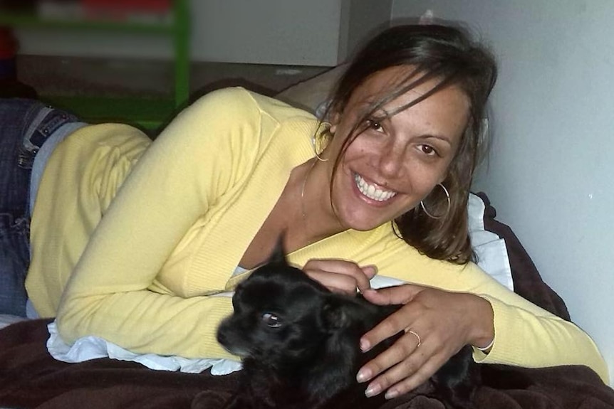 A smiling, bright-eyed woman with dark hair lying down and cuddling a pet.