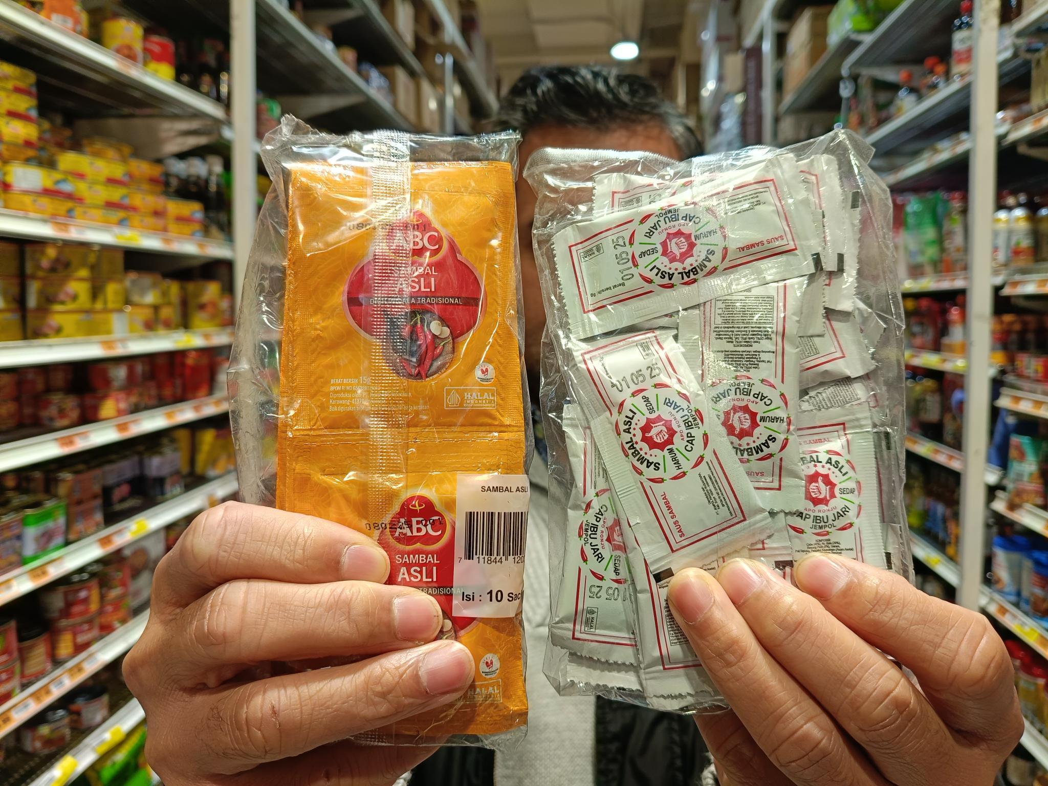 A man handed two packets of chili sauce in sachets towards the camera.