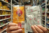 A man handed two packets of chili sauce in sachets towards the camera.
