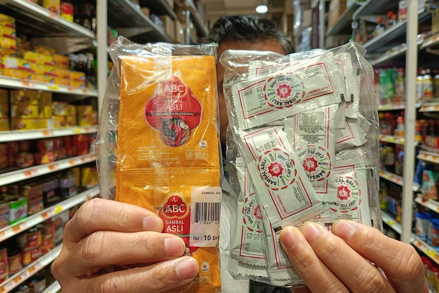 A man handed two packets of chili sauce in sachets towards the camera.