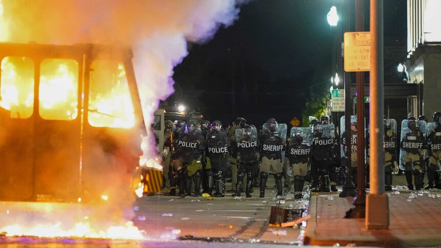 Police stand near a garbage truck ablaze during protests