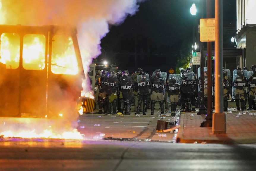 Police stand near a garbage truck ablaze during protests
