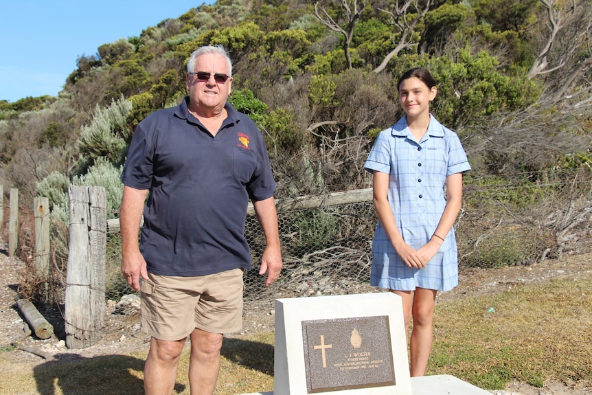 An older man and young girl stand smiling at the camera with a restored grave between them