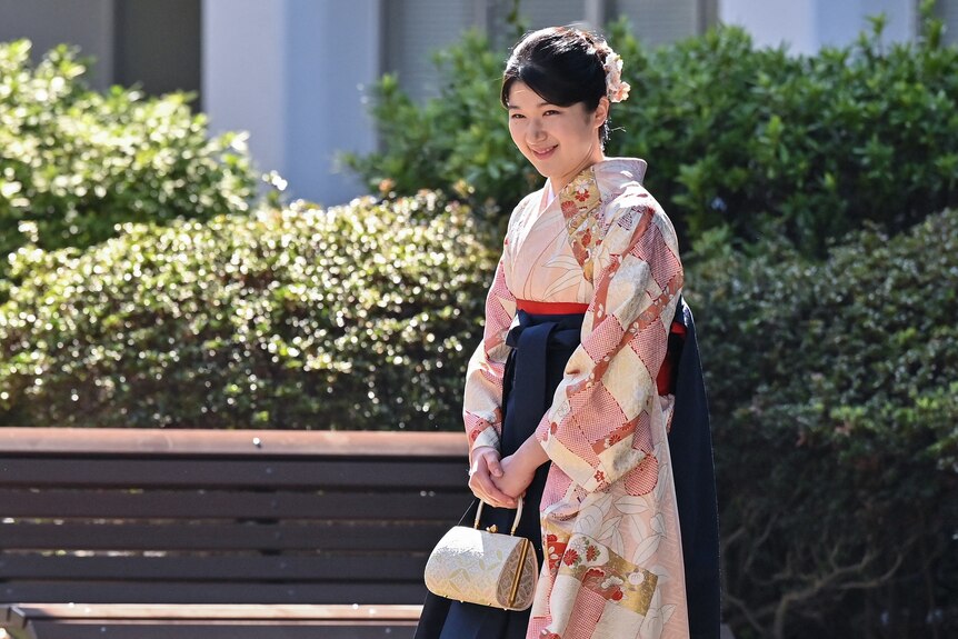 Japan's Princess Aiko wears traditional clothes as she smiles while walking through a garden in the sunlight.