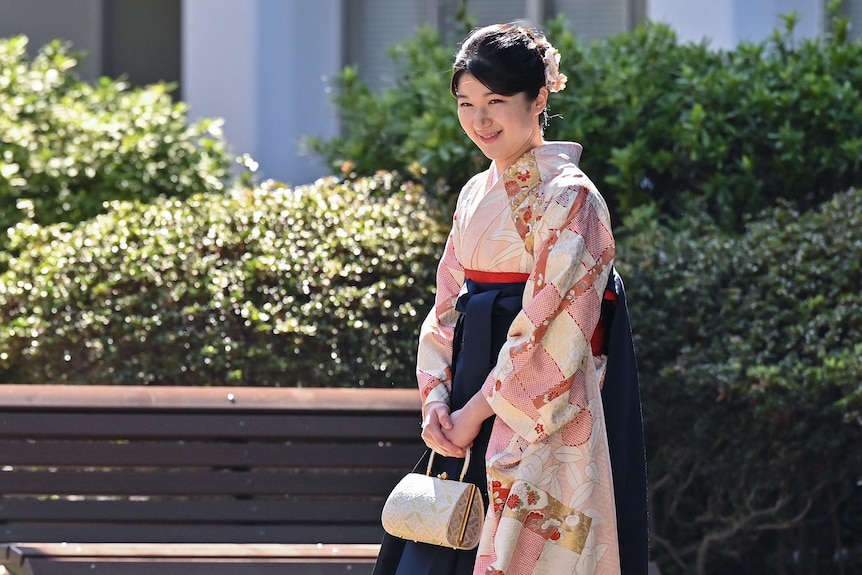 Japan's Princess Aiko wears traditional clothes as she smiles while walking through a garden in the sunlight.