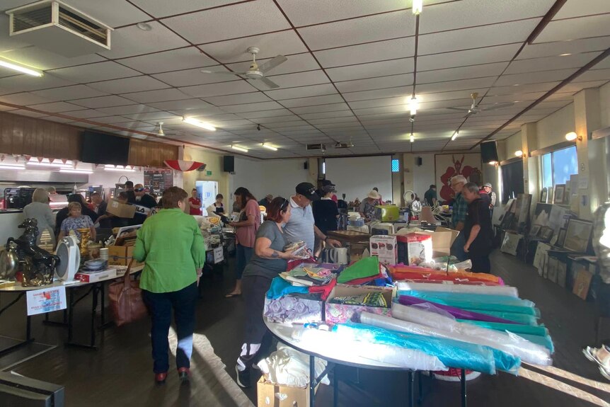 A large group of people at a garage sale looking at a variety of objects on tables and chatting
