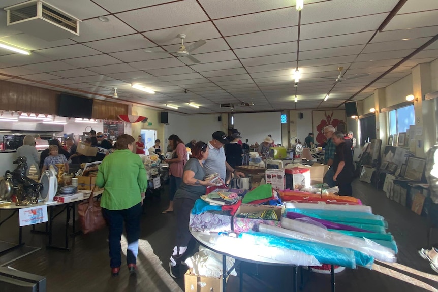 A large group of people at a garage sale looking at a variety of objects on tables and chatting